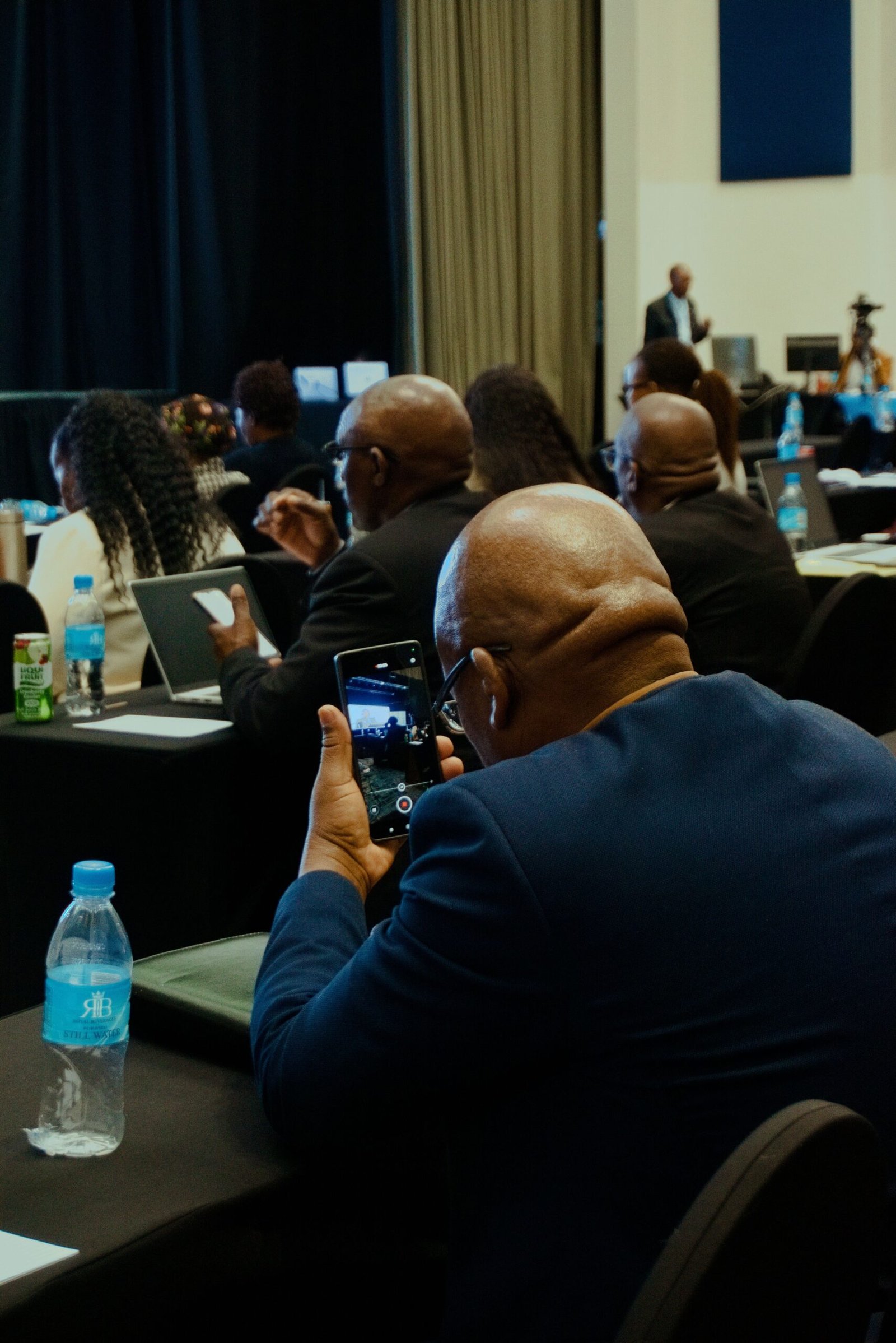 Attendees at a business conference capturing moments on phones for notes and sharing.